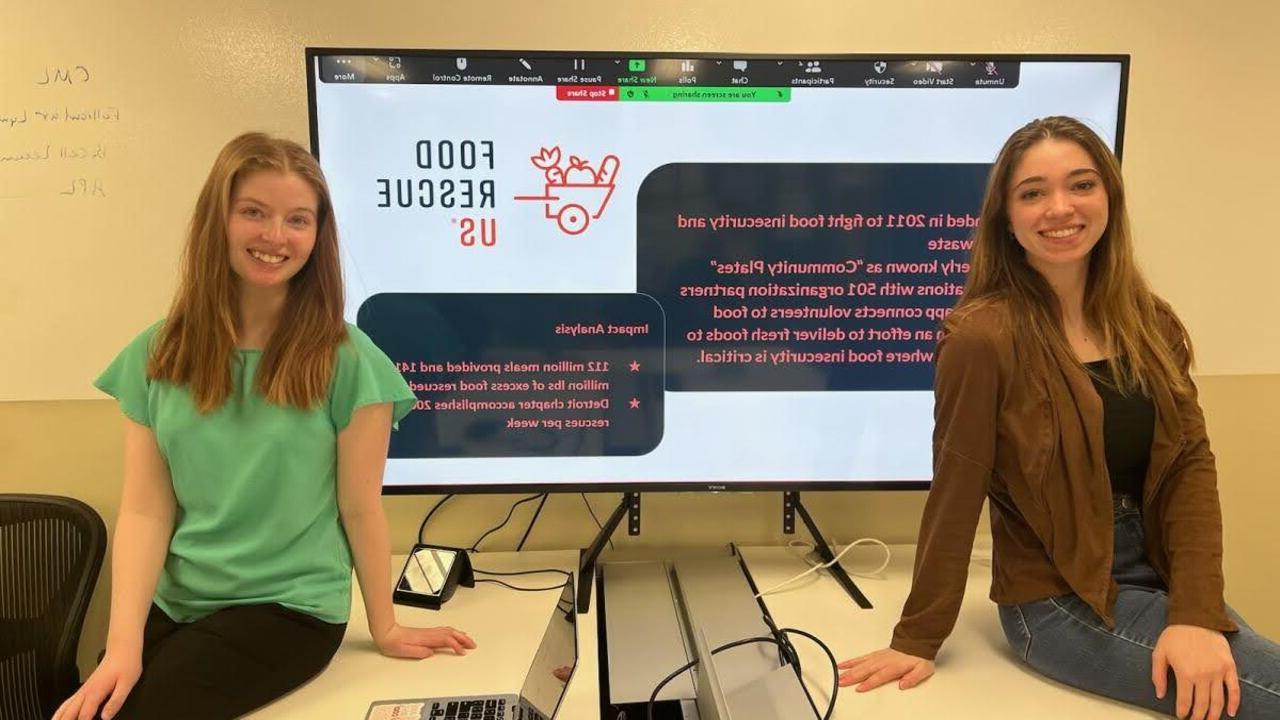 韦德体育app官网学生, 莎拉·奈奎斯特和瑞秋·惠伦, 坐在一个大显示器前，上面显示着美国食品救援组织的信息.